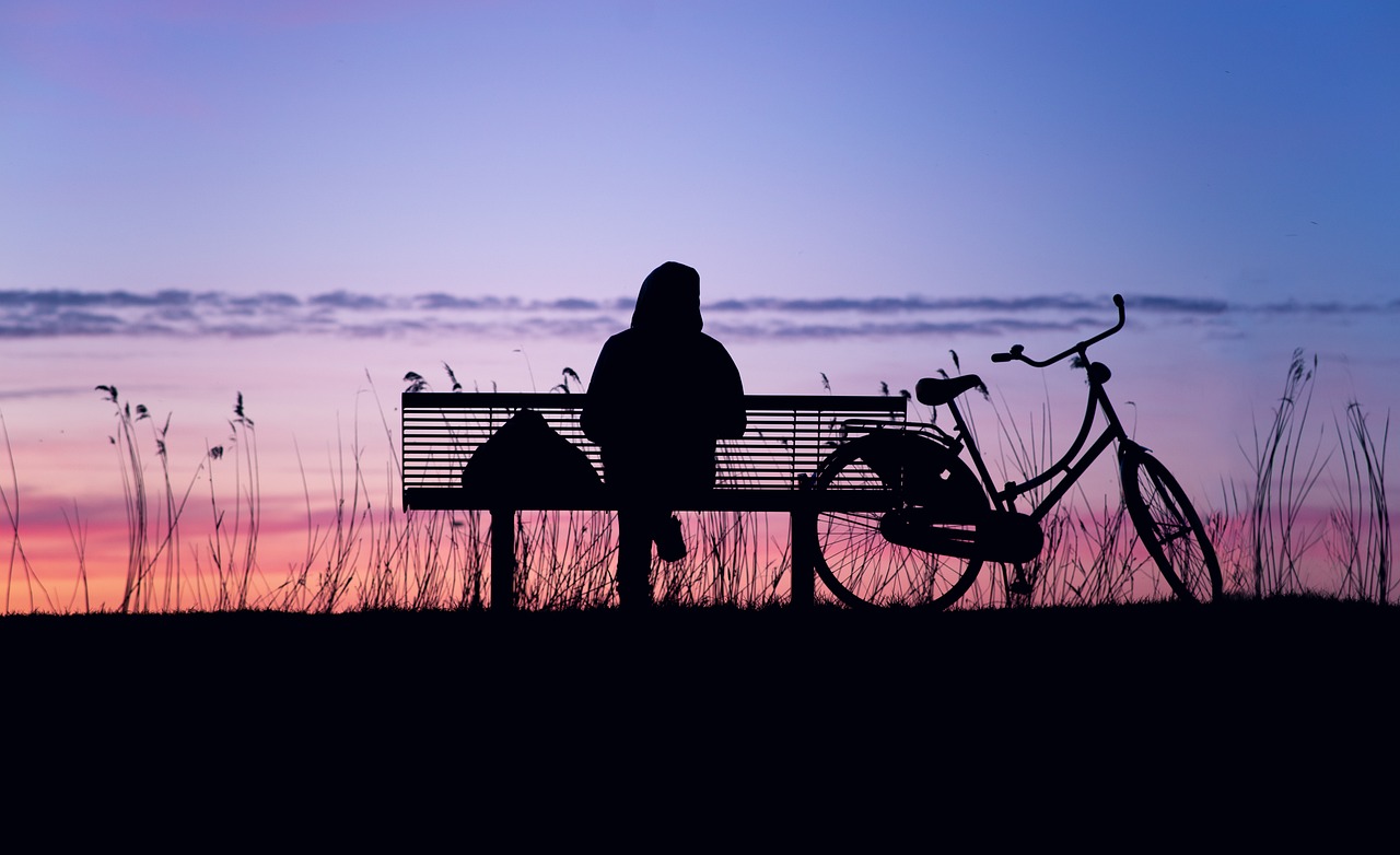 Un cycliste assis sur un banc près de son vélo, et qui assiste au lever de soleil