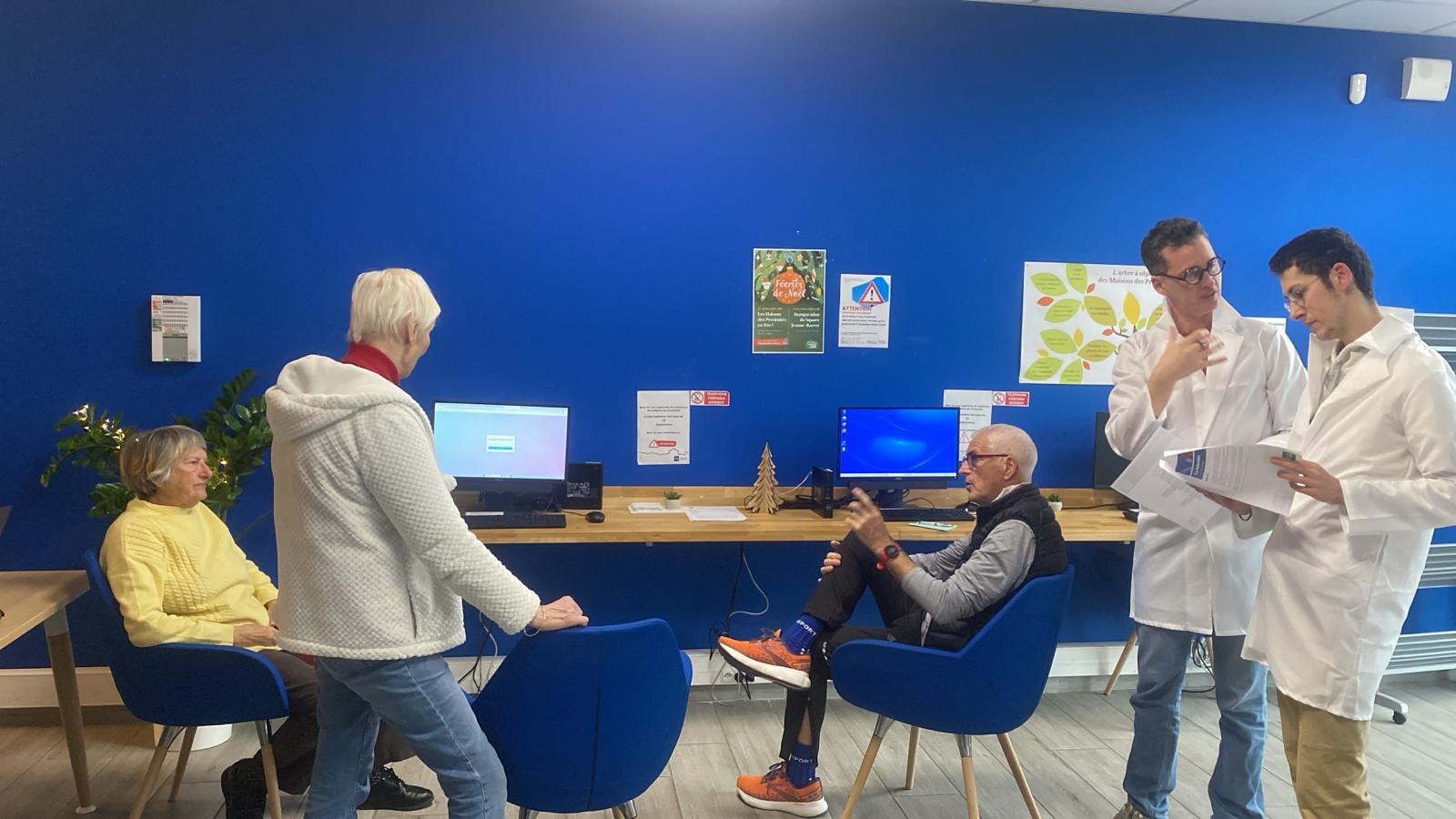 Des personnes debout et assises rassemblées autour d'ordinateurs, dans une salle aux murs et fauteuils bleus