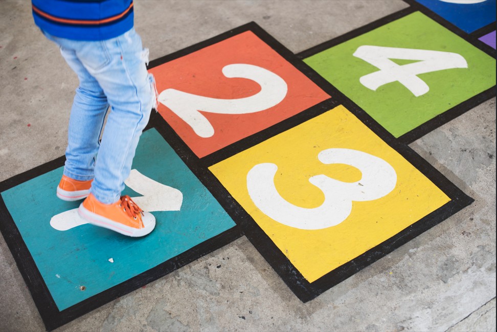 Vue des jambes d'un enfant en baskets orange, jouant à la marelle
