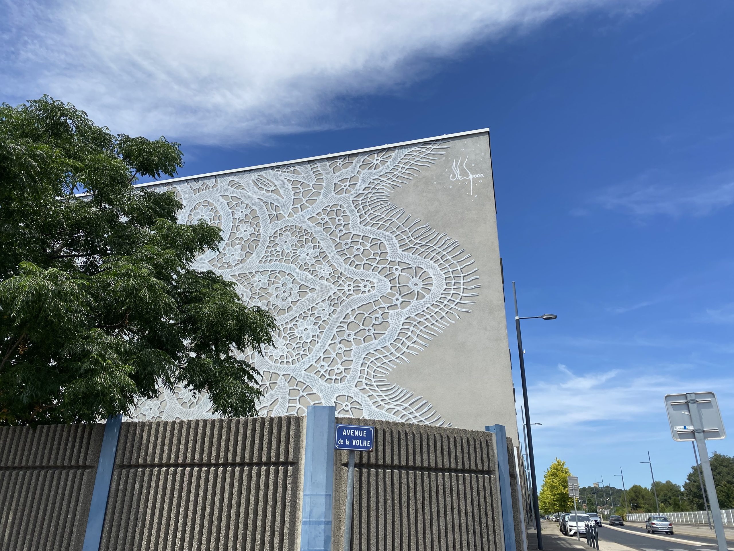 Une oeuvre de treet art sur un mur représentant des dentelles blanches sur fond gris-beige