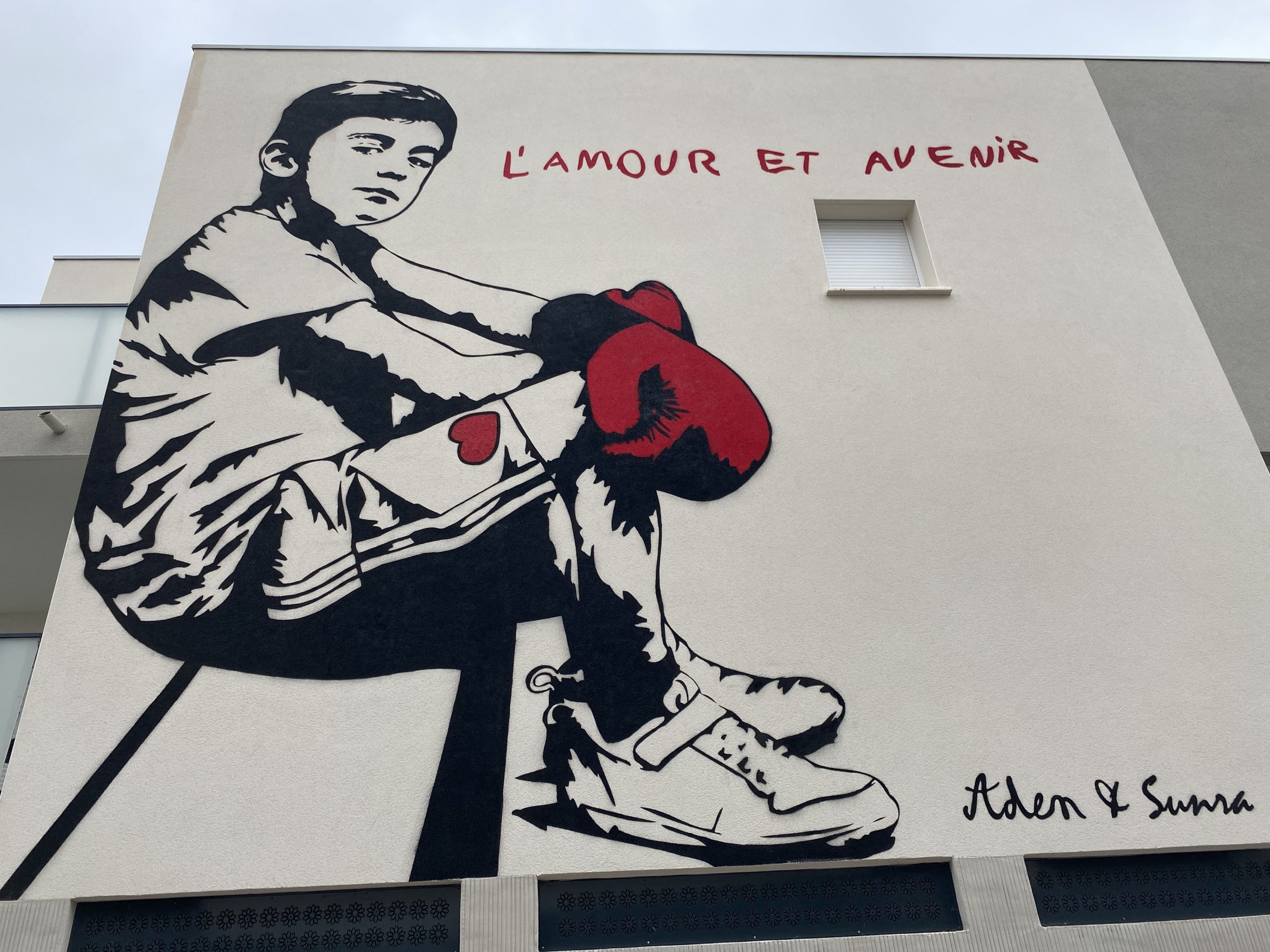 Une fresque représentant un enfant assis avec des gants de boxe aux mains et un cœur sur le short