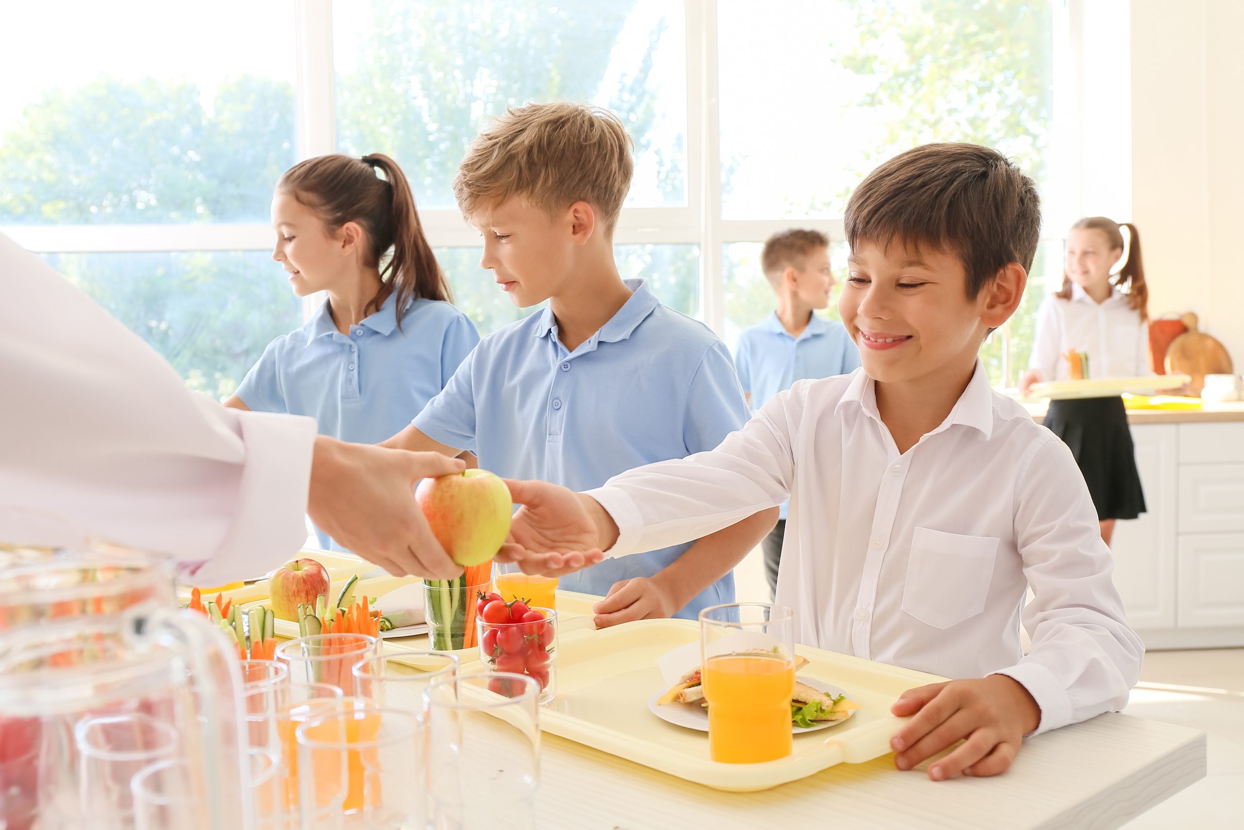 enfants dans un restaurant scolaire, recevant des plats sur leurs plateaux
