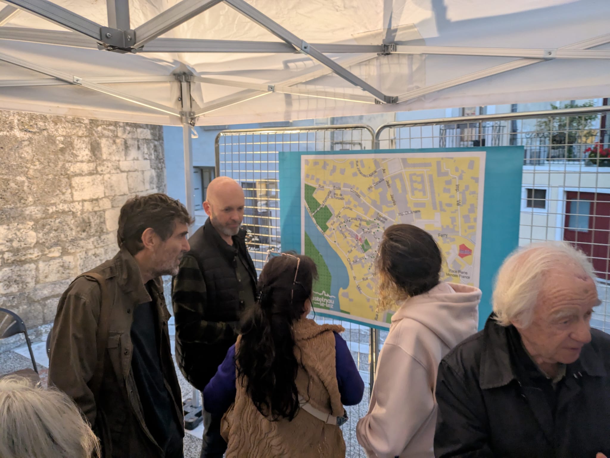 Des riverains du centre ancien de Castelnau-le-Lez examinant une cartographie d'implantation des pots d'Anduze