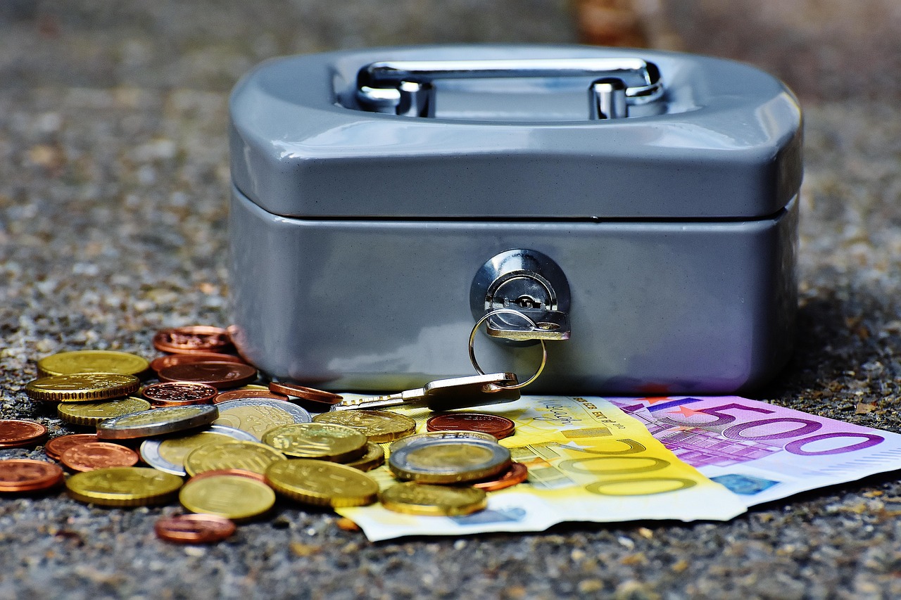 Une petite caisse en fer posée sur une table et entourée de billets et de pièces en euros