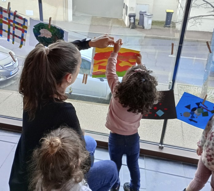 enfants et un adulte accrochant des dessins sur une corde