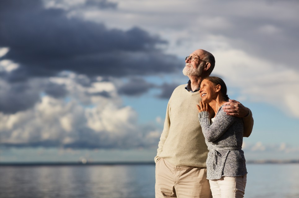 un couple de sexagénaires enlacé, regardant la mer en sourient