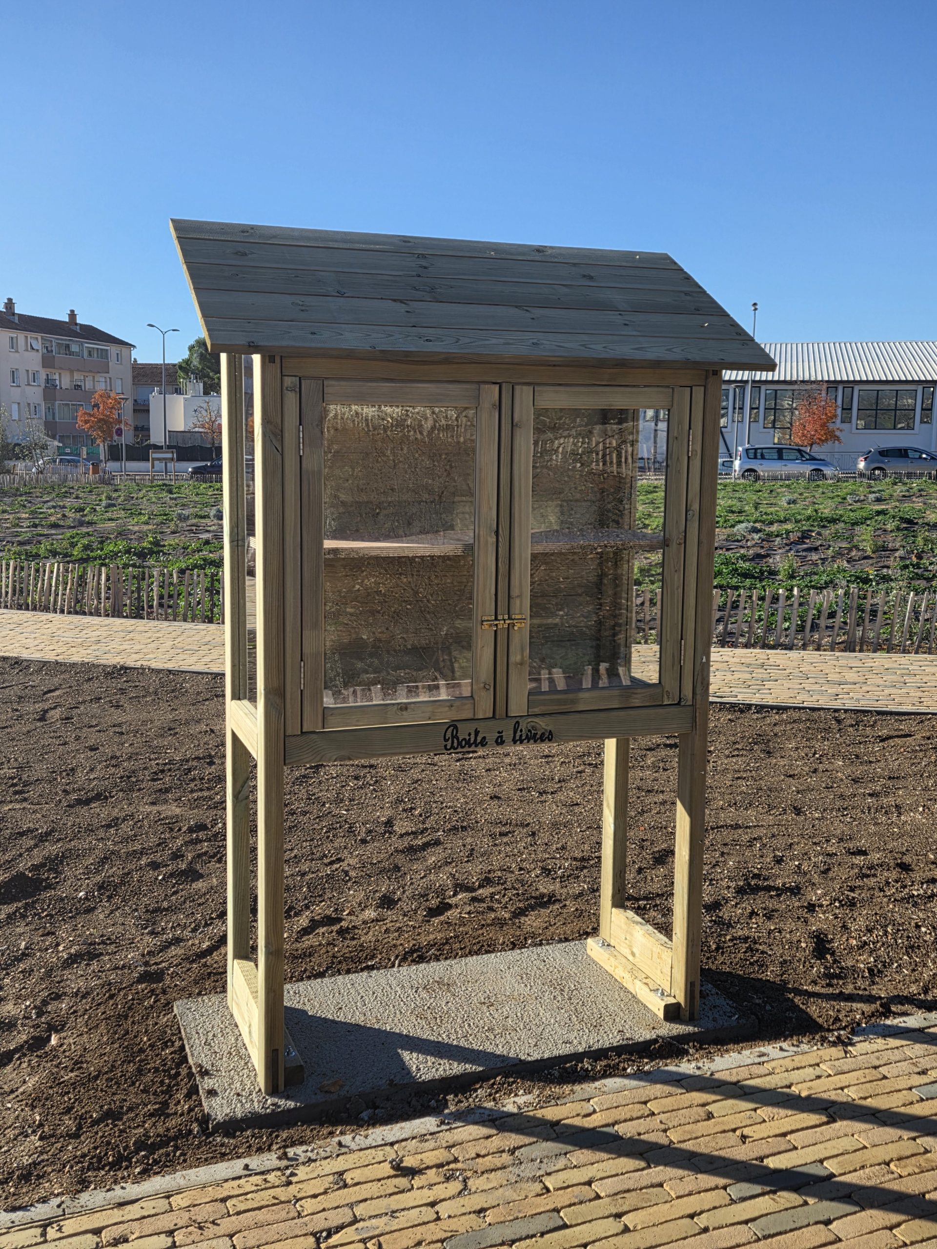 Une boîte à livres en bois, vitrée, installée dans un parc castelnauvien