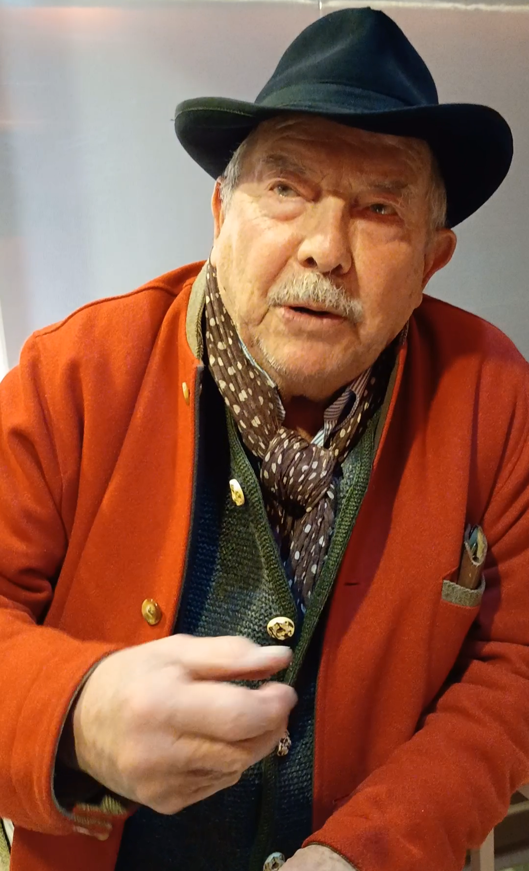 Le peintre Vincent Bioulès portant une veste rouge et un chapeau noir