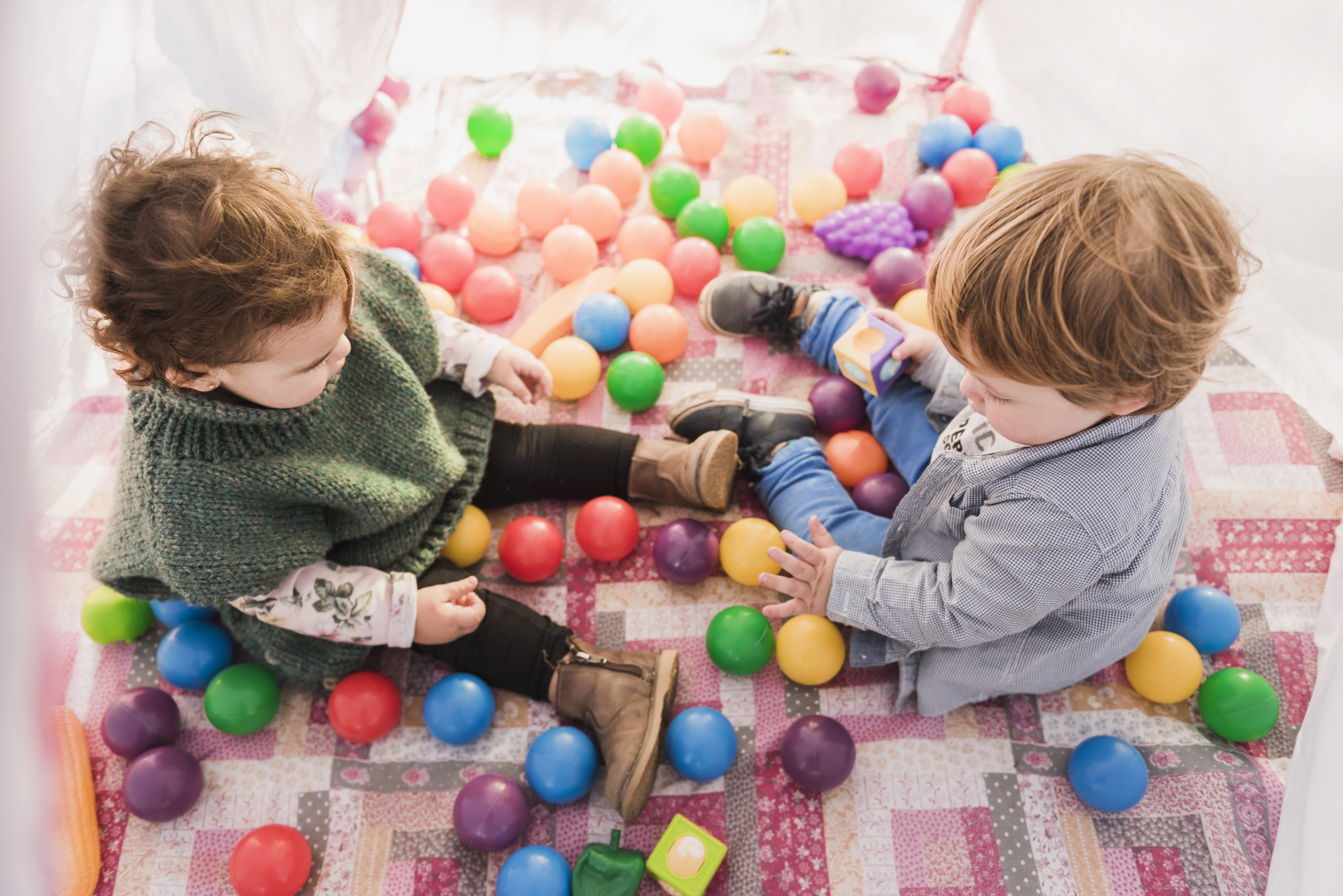 Deux enfants d'environ 3 ans assis parmi des balles de toutes les couleurs