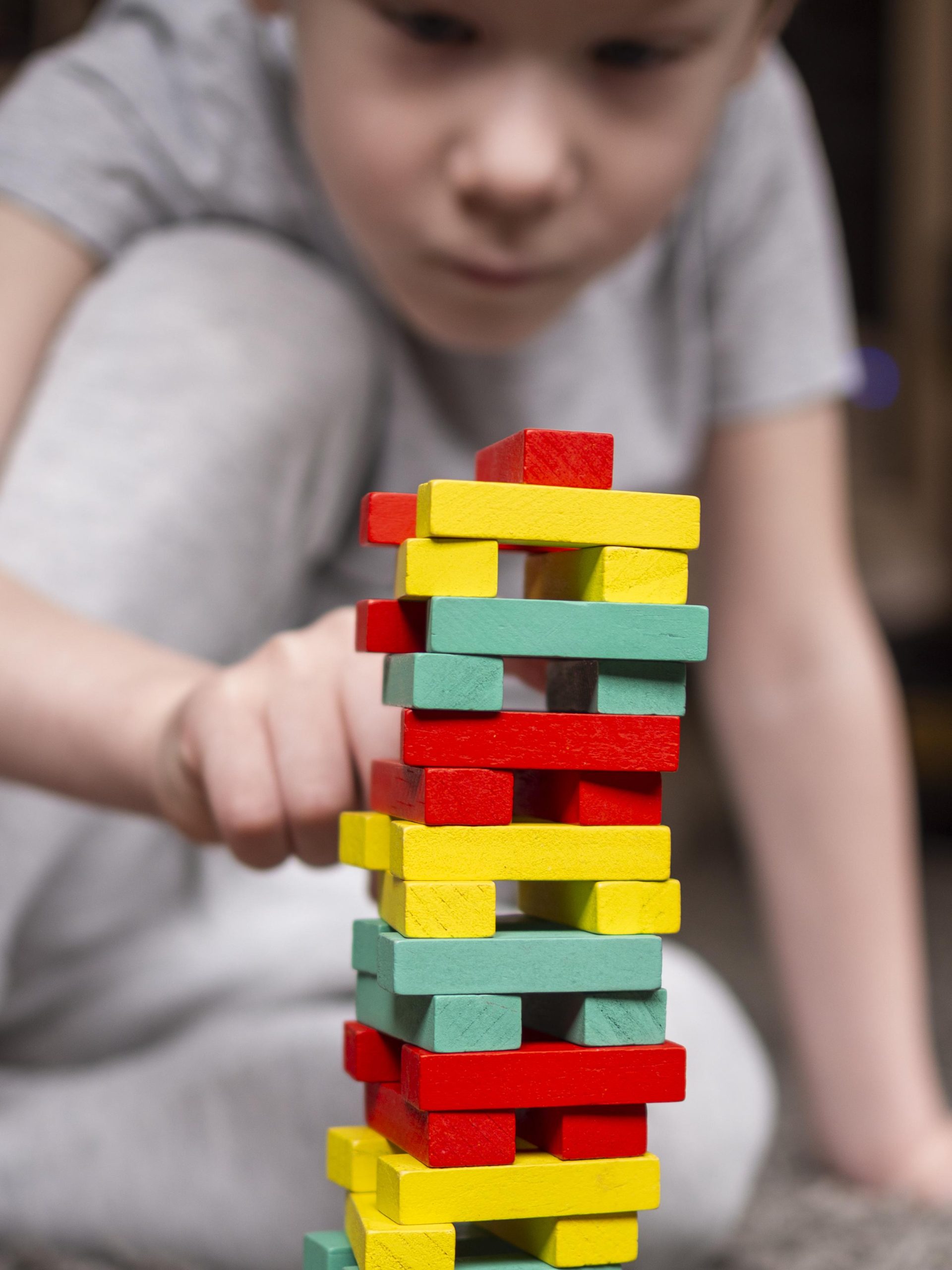 Un garçon d'environ 5 ou 6 ans en train de construire une tour en empilant des plaques en bois colorées
