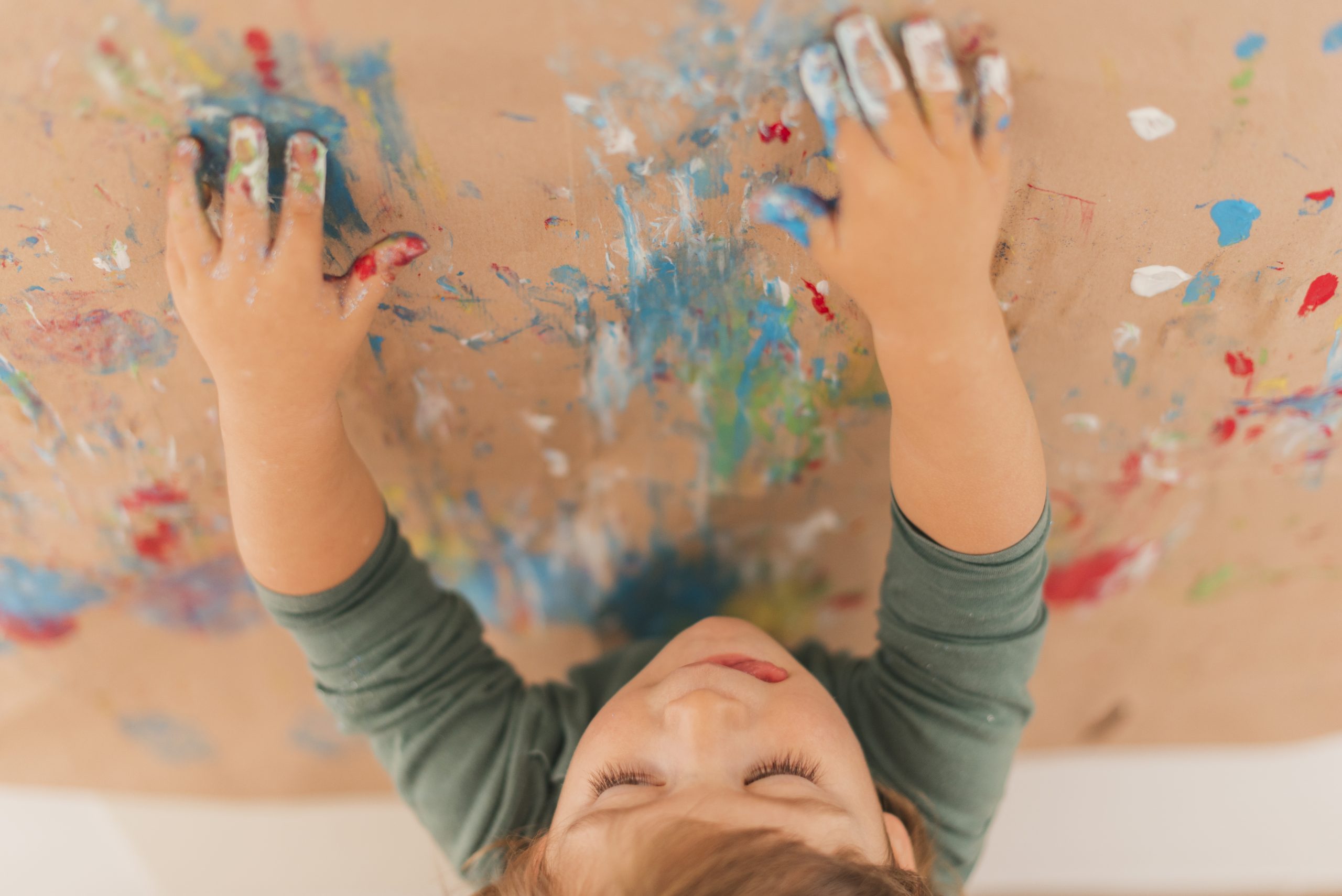 Un petit enfant qui peint avec ses mains, debout devant un panneau recouvert de papier Kraft