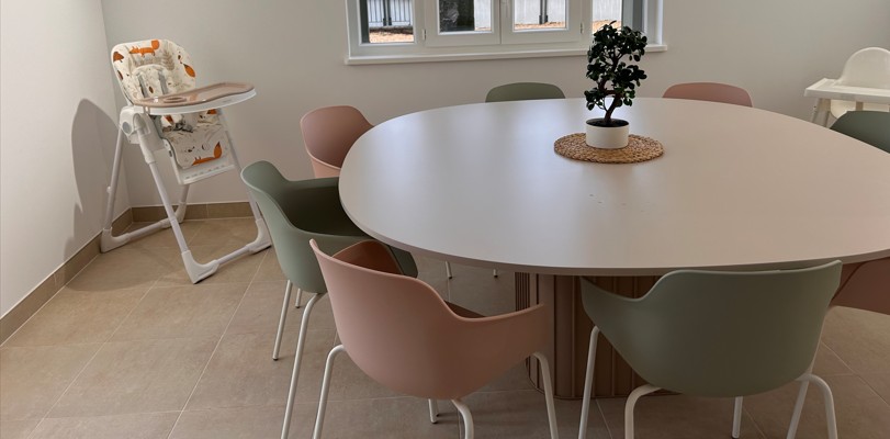 La salle à manger de la Maison d'Olympe, avec sa table beige ronde, entourée de chaises aux couleurs pastels