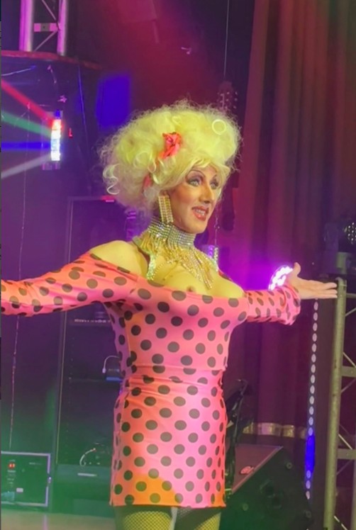 Un homme habillé en femme portant une perruque blonde et une minirobe rose